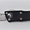 A Microtech Mini Troodon CA Legal OTF Auto Tanto Black Aluminum Handle Knife that is laying on a table.